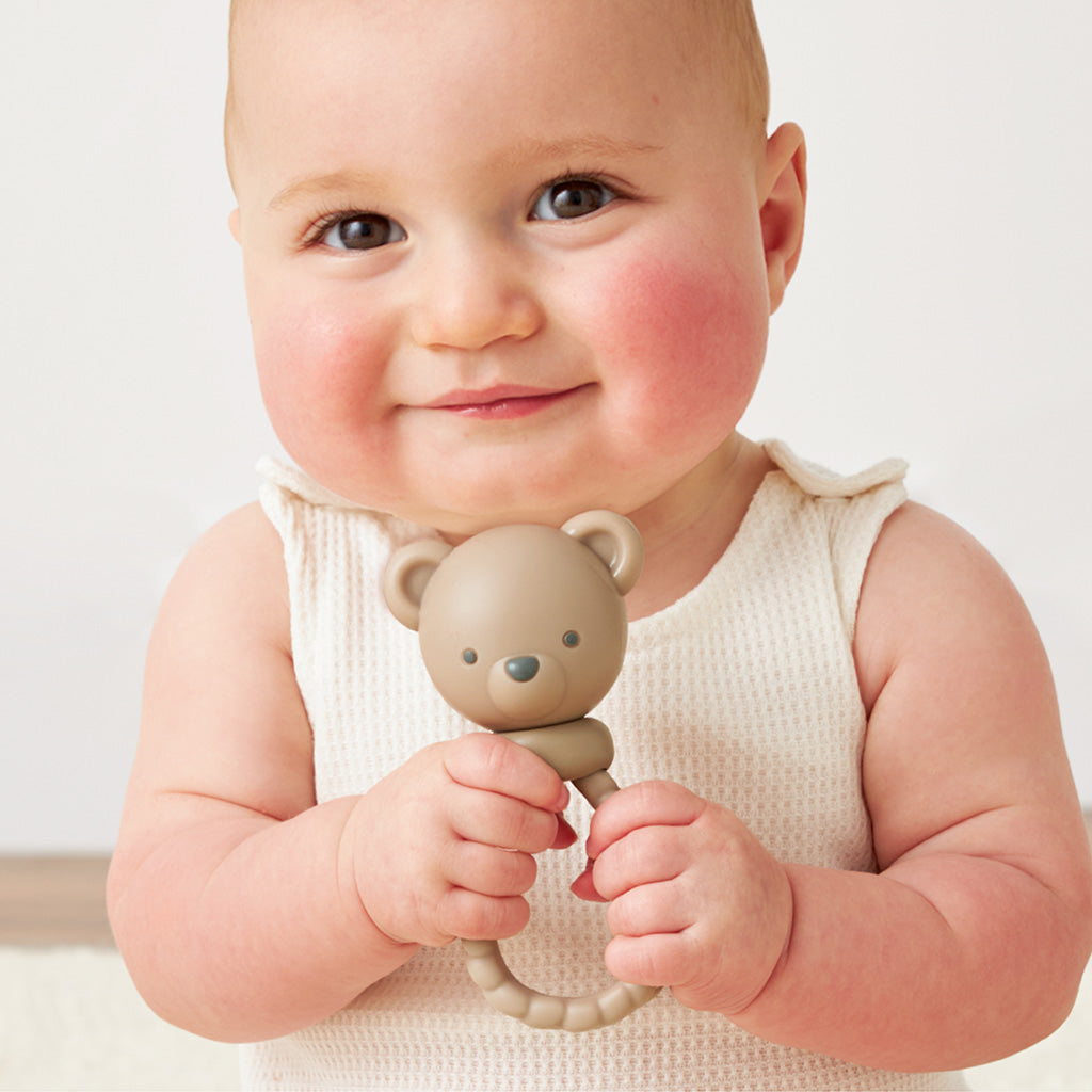 Baby smiles while holding Itzy Ritzy Sweetie Rattle - Theo the Bear