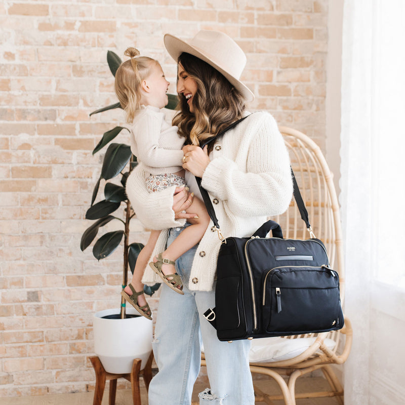 Mom smiles at toddler with JuJuBe Satchel - Black on her shoulder