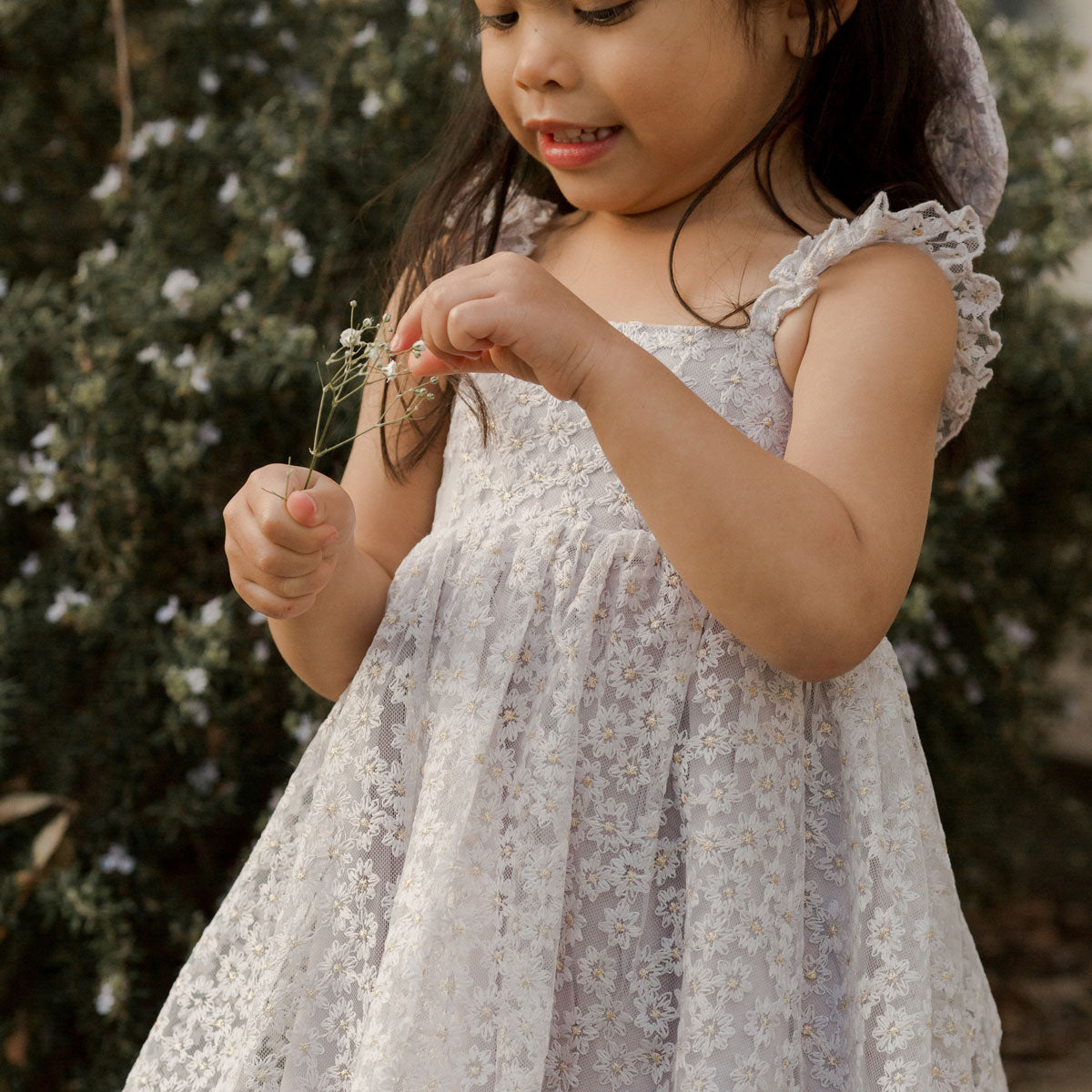 Little girl plays with flower while wearing Noralee Mara Dress - Cloud Daisy Tulle