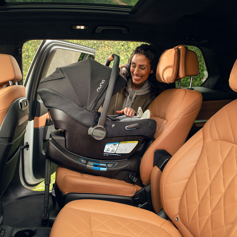 Mom putting Nuna PIPA Aire RX Infant Car Seat with RELX Base - Caviar into vehicle