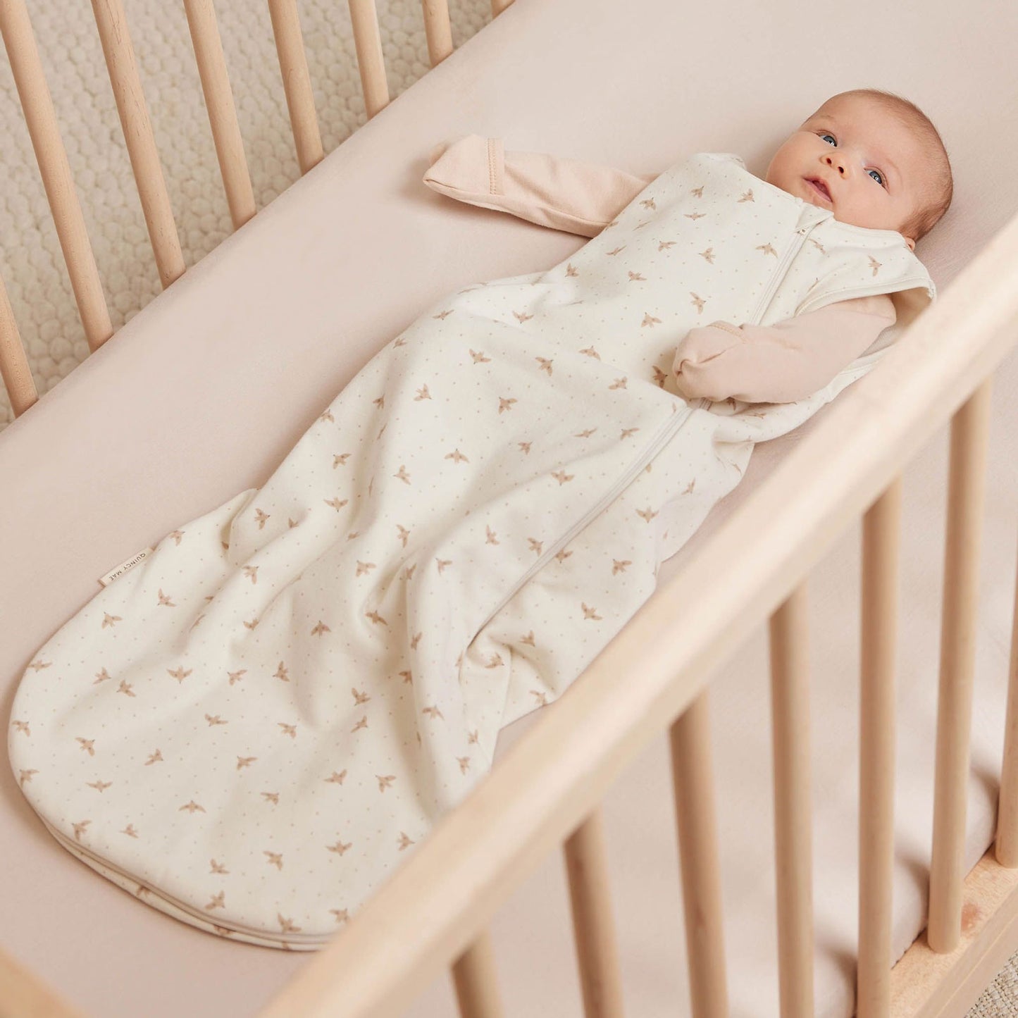 Baby lying in crib wearing Quincy Mae Jersey Sleeping Bag - Doves - Ivory