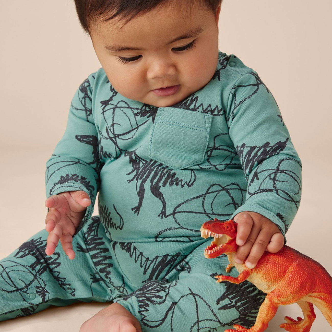 Baby playing with dinosaur toy while wearing Tea Collection Long Sleeve Pocket Baby Romper - Scribbled Dinosaurs