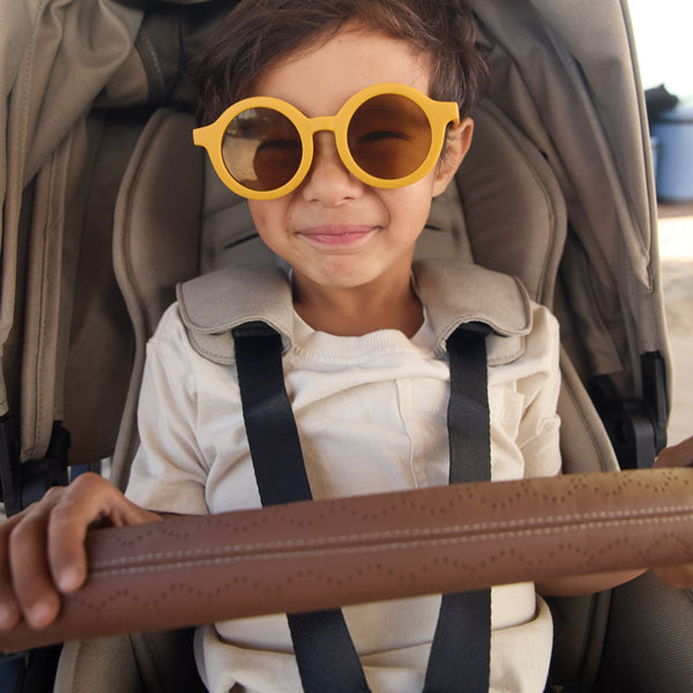 Child wearing sunglasses smiles while riding in Veer Switchback with Veer Switchback Seat Bumper Bar Leather Grips - Genuine Napa Leather - Saddle attached