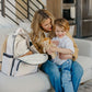 Witney Carson holding son while sitting next to JuJuBe Classic Backpack - Witney Carson - Cloud