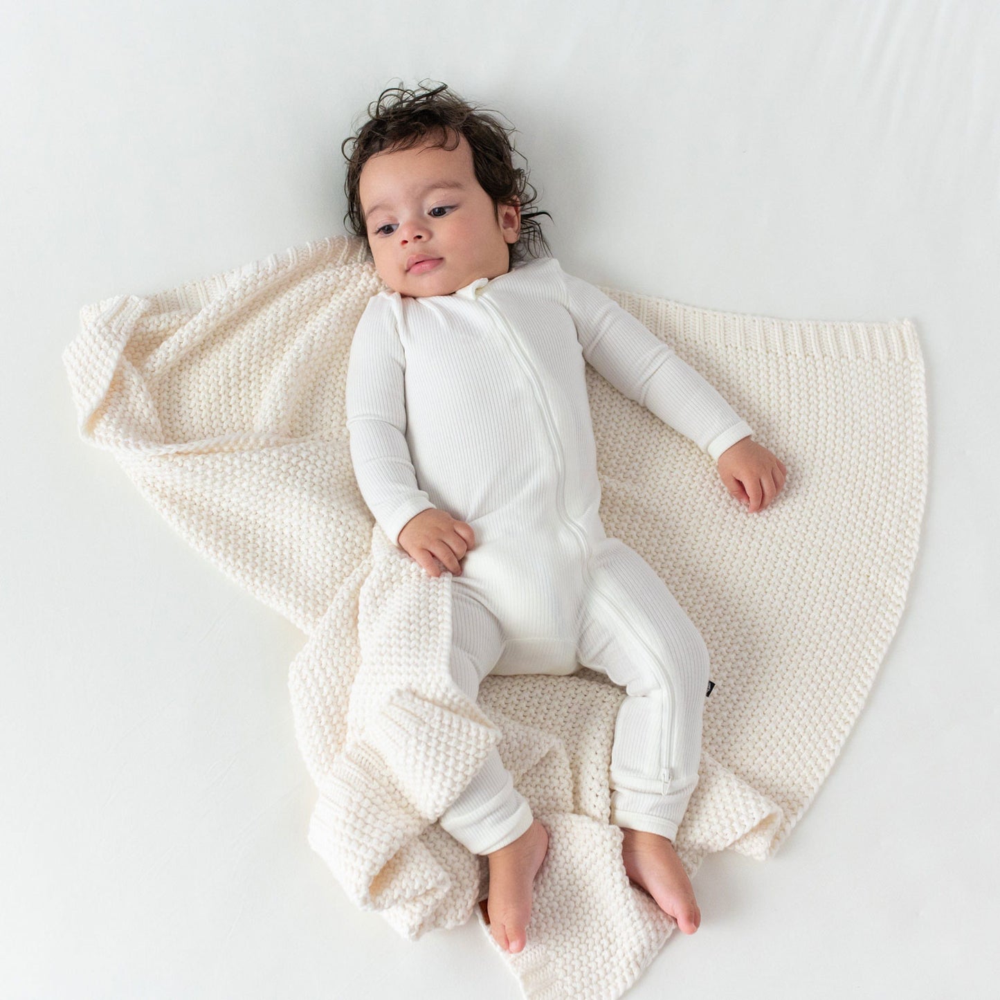 Baby lying on Kyte BABY Chunky Knit Baby Blanket - Cloud