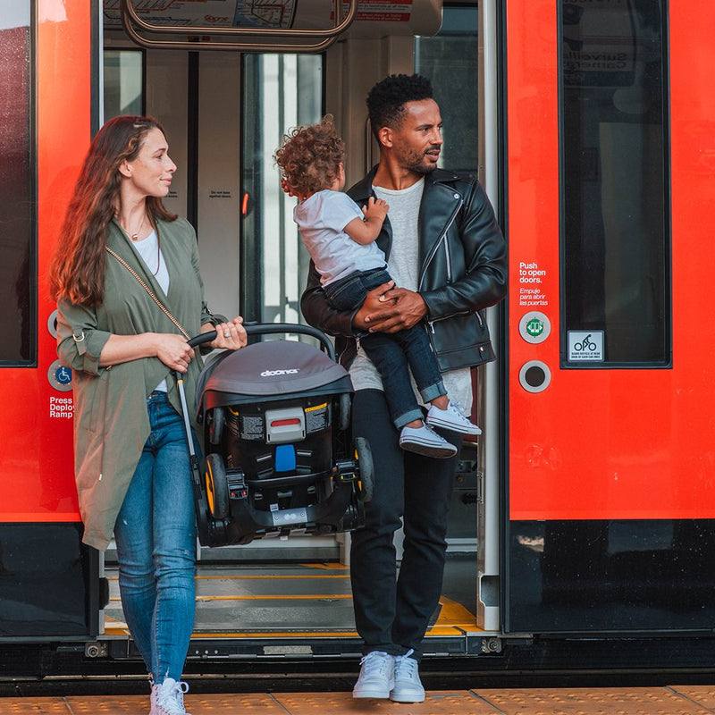 Parents carry Doona Infant Car Seat and Stroller off train