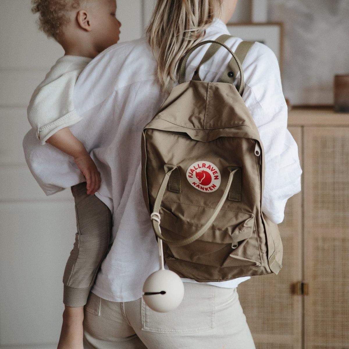 Mom using Mushie Silicone Pacifier Holder Case - Shifting Sands on Fjallraven backpack