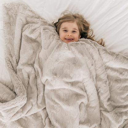 Little Girl laying in Saranoni Patterned Faux Fur Throw Blanket - Feather