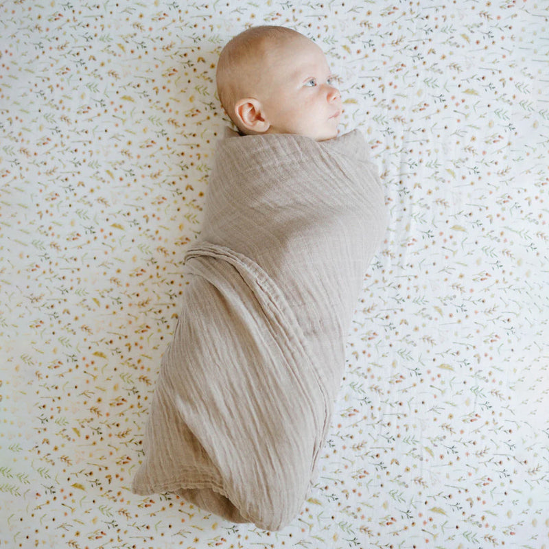 Baby laying on Little Unicorn Organic Cotton Muslin Crib Sheet - Floral Field