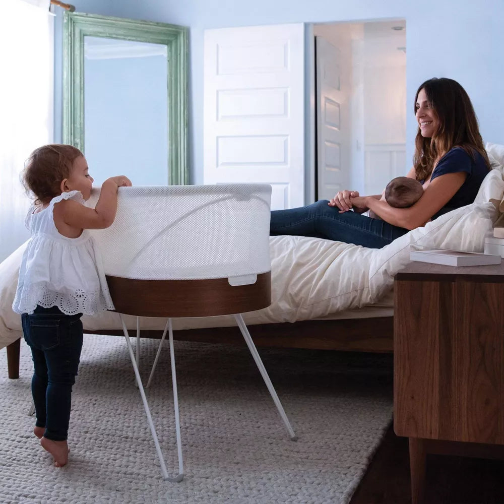 Mother in bedroom sits by Happiest Baby SNOO Smart Sleeper - White