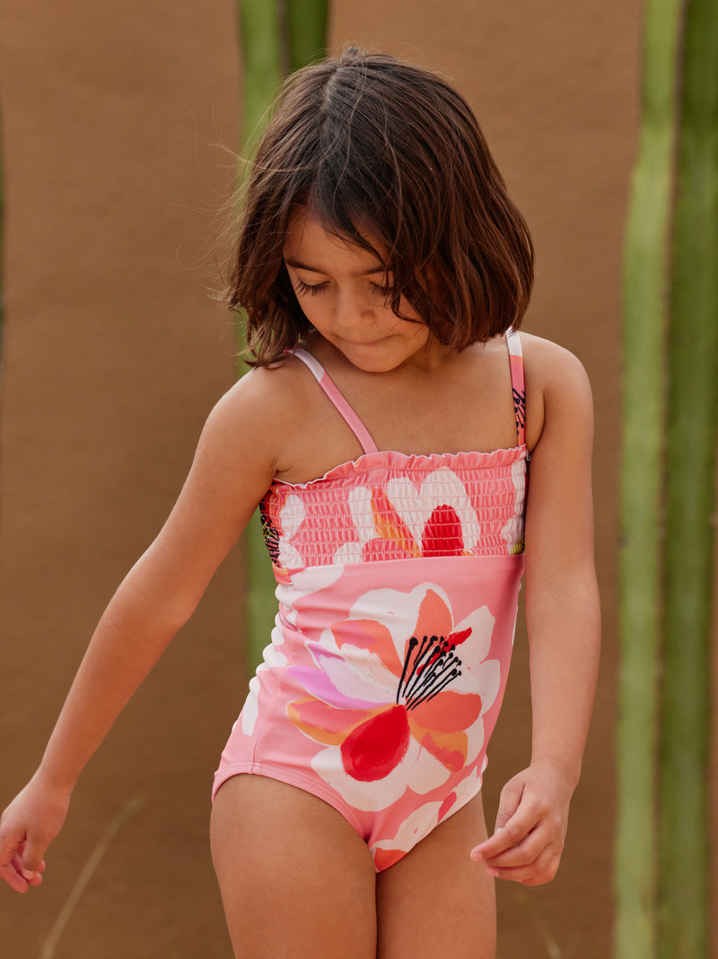 Girl wearing Girl sits by pool wearing Tea Collection Smocked One-Piece Swimsuit - Floral Burst 