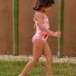 Girl walking wears Girl sits by pool wearing Tea Collection Smocked One-Piece Swimsuit - Floral Burst 