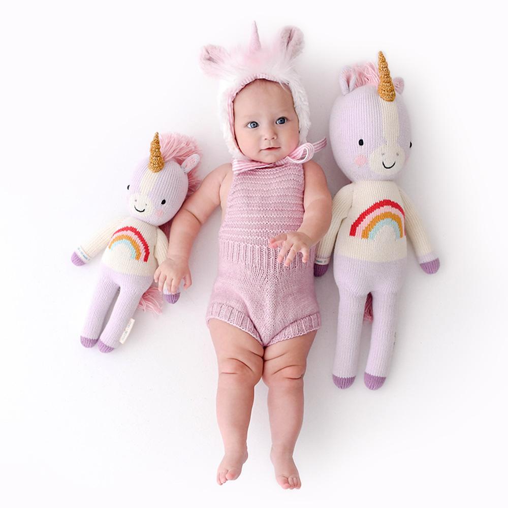 Baby wearing unicorn bonnet and lying next to Cuddle and Kind Zoe the Unicorn